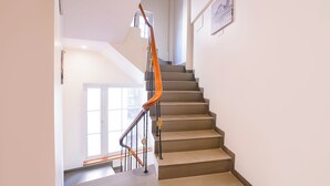 A staircase with a wooden handrail and beige steps, leading to a landing with a window and a framed picture on the wall. - Fabhotel Mumbai Corporate Rooms Jb Nagar (Mumbai)