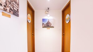 A hallway with wooden doors, a ceiling-mounted light fixture, and a framed picture of a building. - Fabhotel Mumbai Corporate Rooms Jb Nagar (Mumbai)