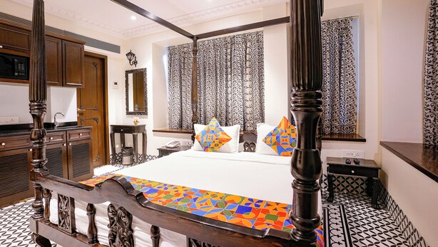 A four-poster bed with a colorful geometric bedspread, a wooden nightstand, a mirror, and patterned curtains. - Fabhotel Mumbai Corporate Rooms Jb Nagar (Mumbai)