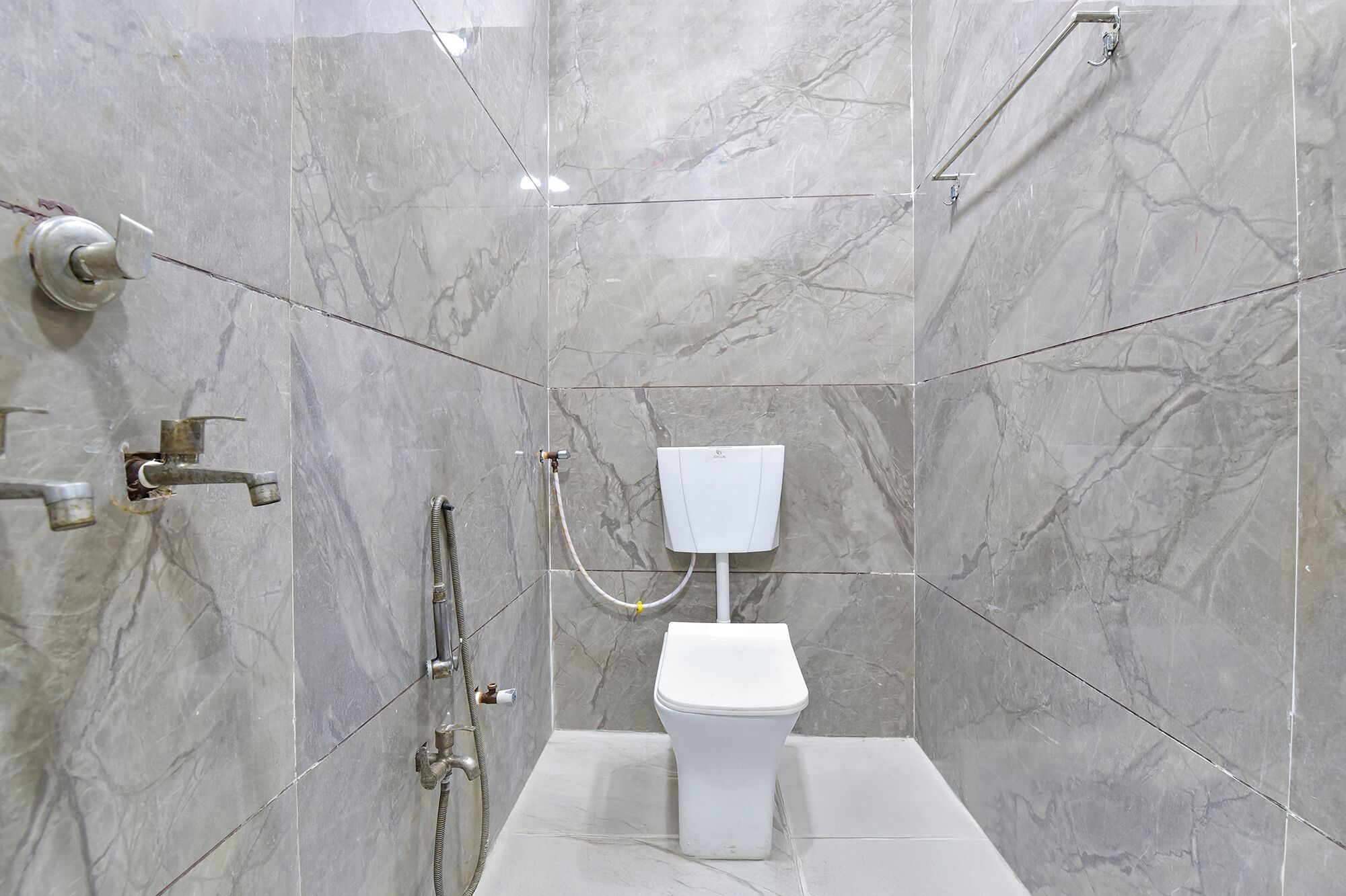 Een moderne badkamer met een wit toilet, een douche met een handdouche en een wandmengkraan.