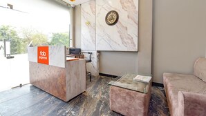 Un'area di accoglienza con parete in marmo, un orologio, una reception e un angolo salotto con tavolino in vetro.