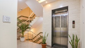 A modern elevator with a digital display, a staircase with metal railings, and potted plants on the floor.