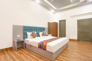 A modern bedroom with a large bed, a nightstand, a wardrobe, and two doors. - FabHotel Villa The Suites (Prayagraj)