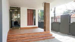 Un área de recepción con puerta de vidrio, un conjunto de escalones de madera que conducen a una entrada cubierta y vistas al exterior.