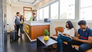 Zona de recepción de un hotel con un mostrador de madera, una mesa con computadora y un área de descanso con mesa y sillas.