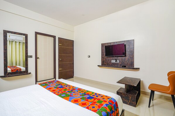 A hotel room with a bed, a TV mounted on the wall, a desk, and a chair. - Fabhotel Green Vista (Bangalore)