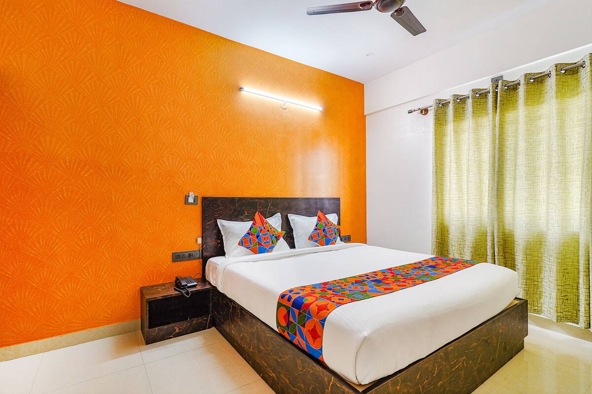 Une chambre d’hôtel avec un grand lit, une table de chevet, un ventilateur de plafond et une fenêtre avec des rideaux.