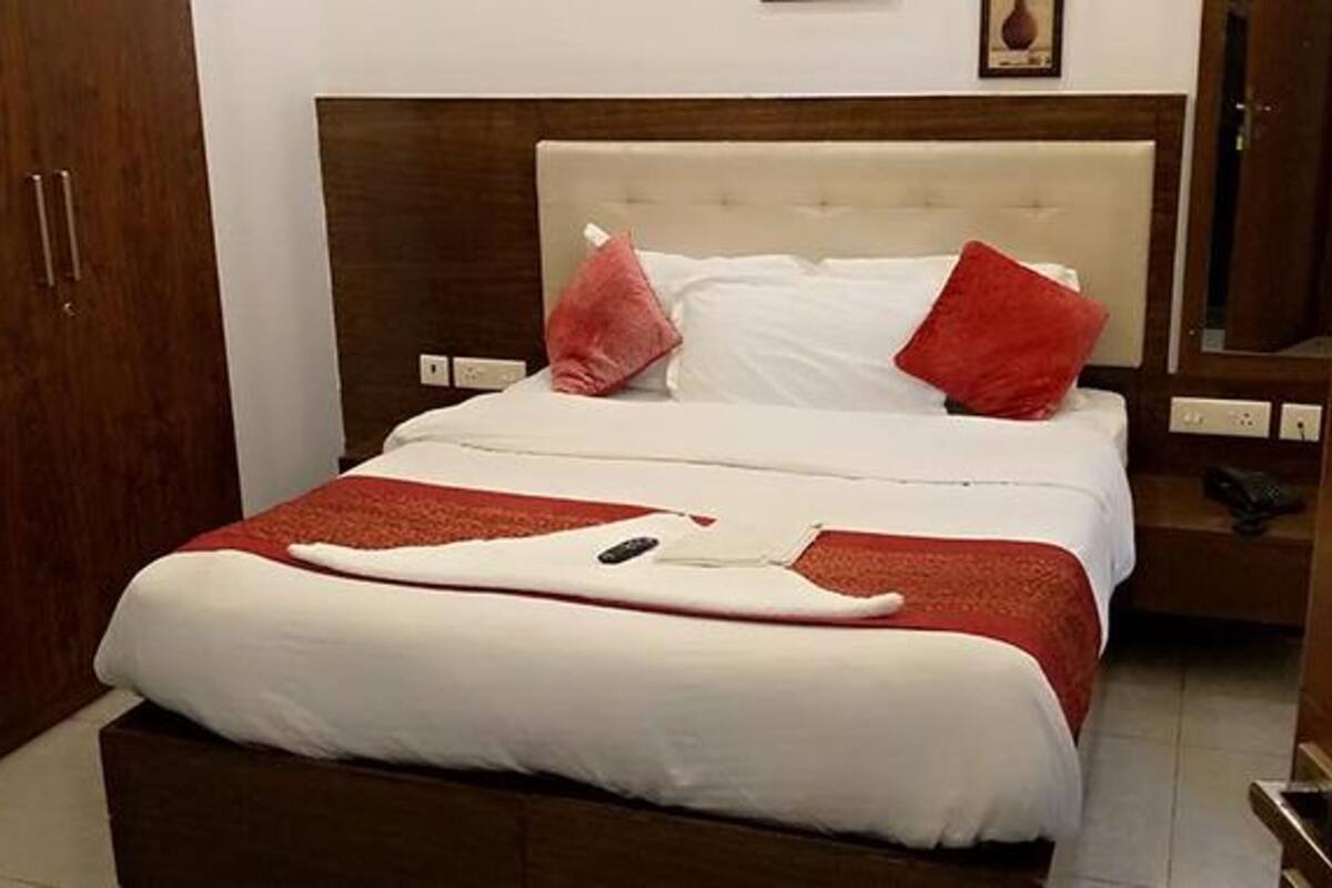 Ein ordentlich bezogenes Bett mit weißer und roter Bettwäsche, ein hölzerner Kopfteil und ein kleiner Nachttisch mit Lampe.
