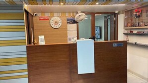 A reception desk with a clock, calendar, and a sign indicating a reception area. - Fabhotel Casa De Grand (Prayagraj)