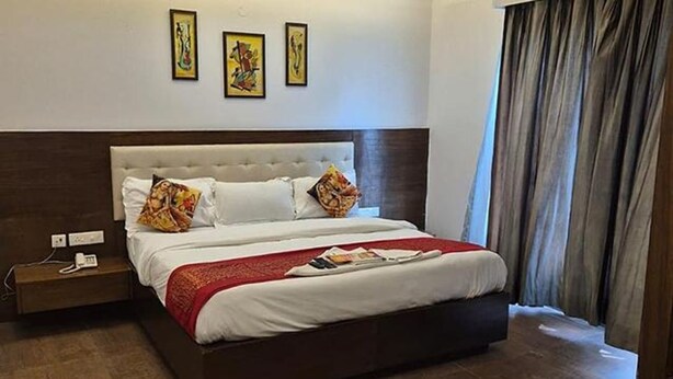 A hotel room with a large bed, a nightstand, and three framed artworks on the wall. - Fabhotel Casa De Grand (Prayagraj)