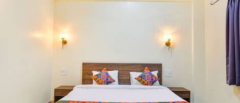 A hotel room with a bed, two nightstands, a wooden headboard, two wall-mounted lights, and a window with curtains.