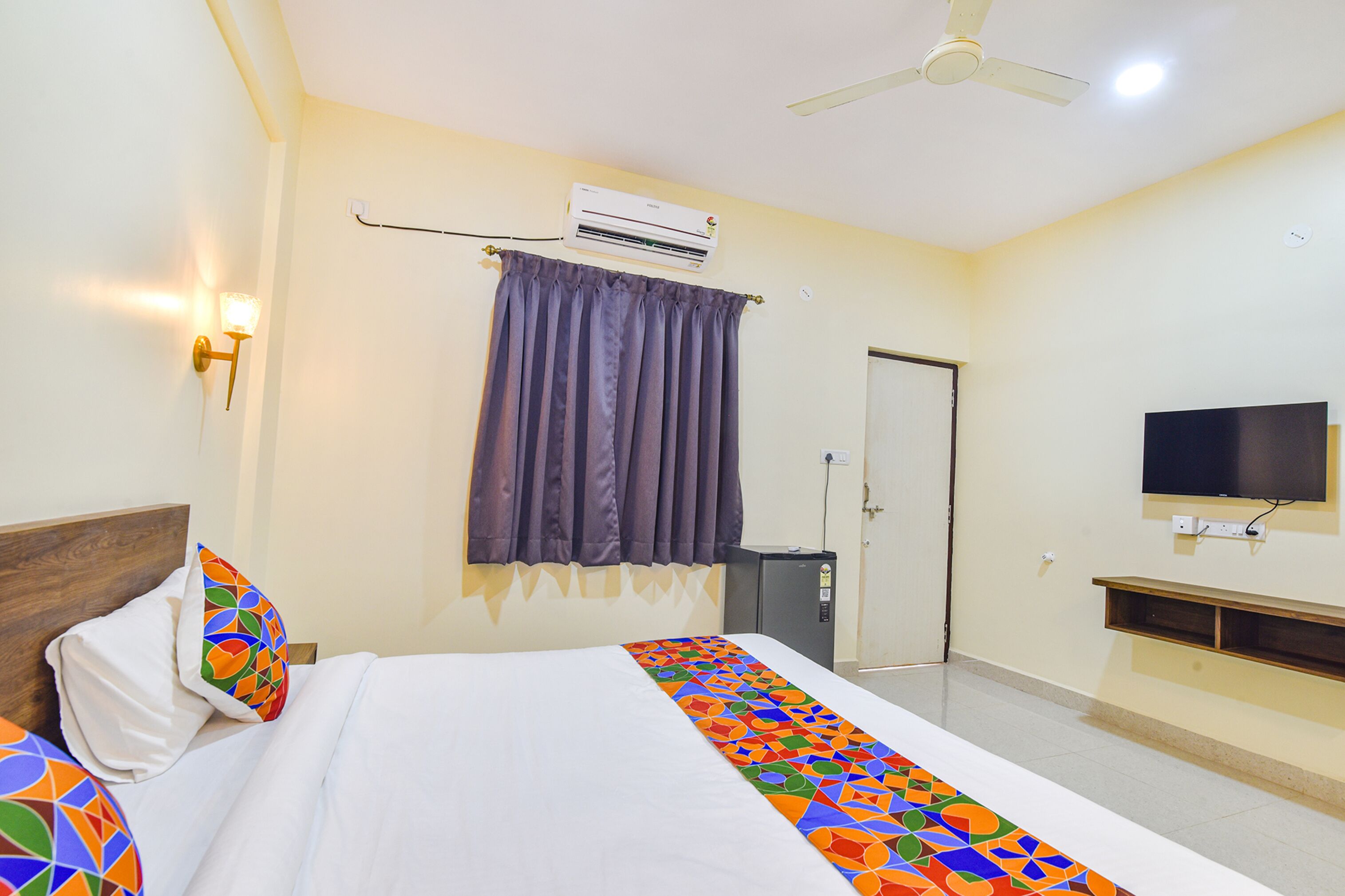 A hotel room with a bed, an air conditioner, a television, and a ceiling fan.