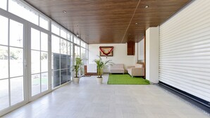 Um corredor amplo com grandes janelas, área com grama sintética verde e teto de madeira.