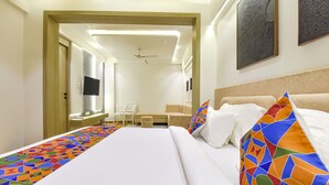 Quarto de hotel com uma cama grande, um sofá, uma televisão e uma pequena mesa com cadeiras.