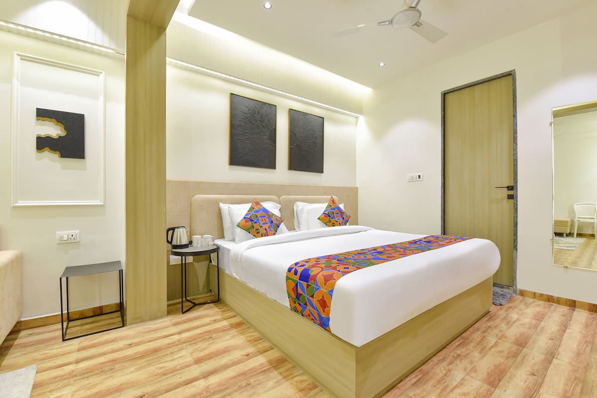 A hotel room with a large bed, a bedside table with a kettle, two wall-mounted artwork pieces, and a door with a mirror.