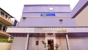 Un hôtel appelé « Dhan Laxmi Residency », avec une enseigne en langue locale, une enseigne bleue indiquant qu’il fait partie du réseau « fab hotels », et une entrée moderne agrémentée de plantes en pot.
