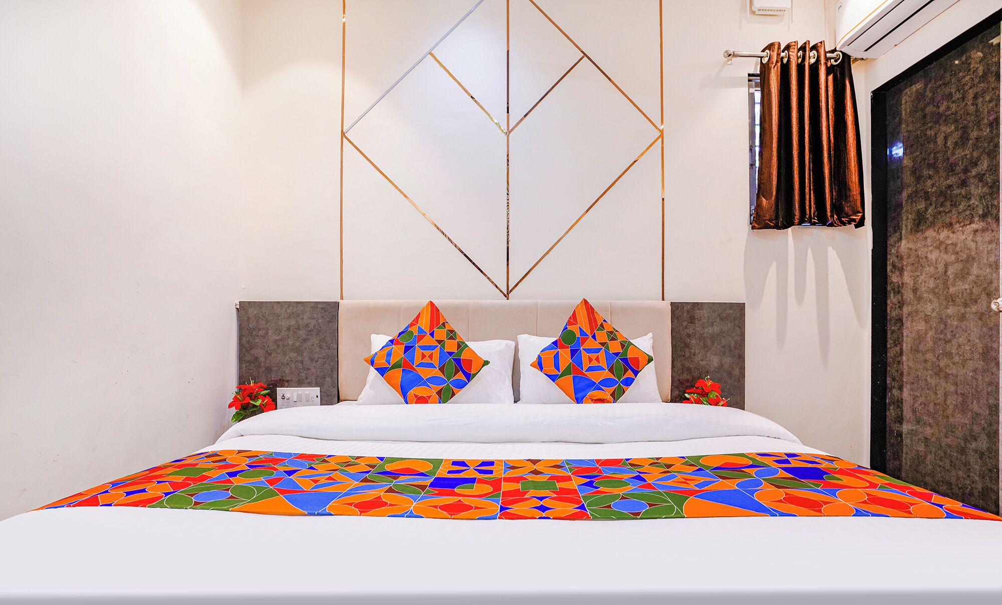 Una habitación de hotel moderna con una colcha de diseño geométrico, un cabecero en tonos neutros y un panel decorativo en la pared.