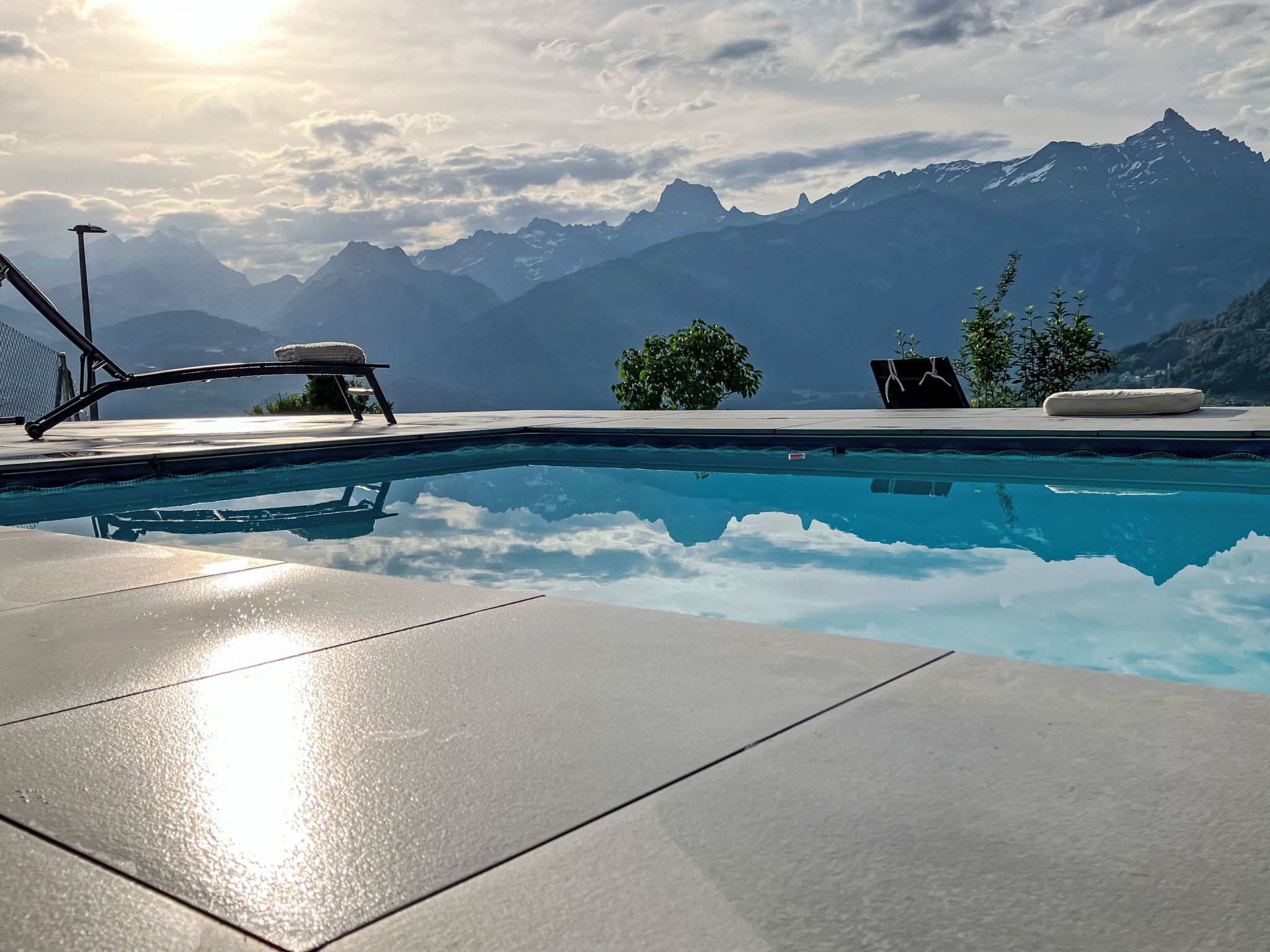 A swimming pool with a mountain view, lounge chairs, and a sunshade.