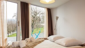 A bedroom with a bed, a window with curtains, a lamp, and a view of a park. - Lau'tentik by Interhome (Collombey-Muraz)
