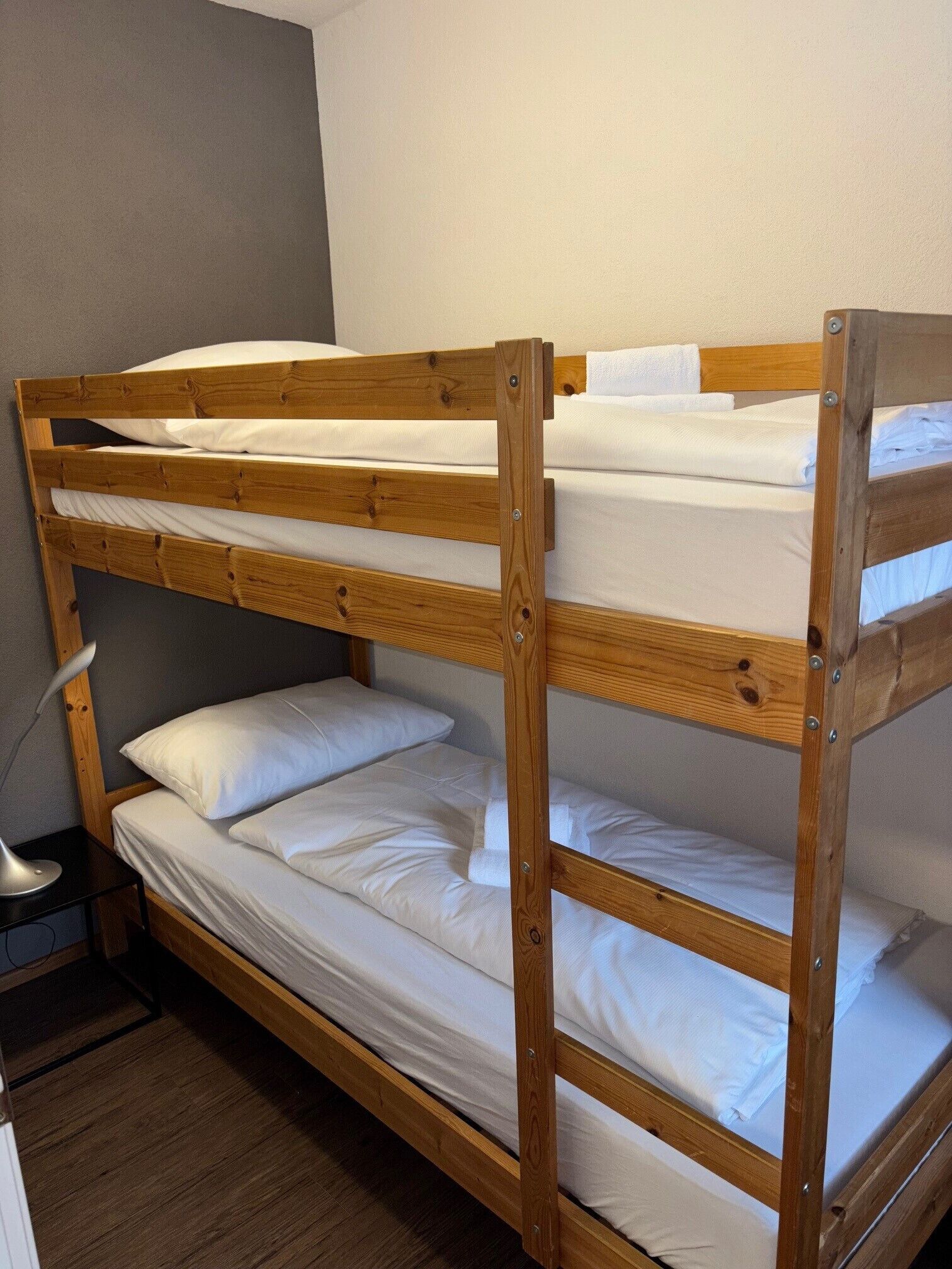 A bunk bed with three levels, a bedside table, and a lamp.