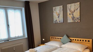 Una cama bien hecha con ropa blanca y toallas, un cabecero de madera, una mesita de noche con lámpara y dos cuadros de ciervos colgados en la pared.