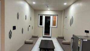 A room with a central table, two sofas, a ceiling fan, and a refrigerator. - Hotel Sky MMD (Jaipur)