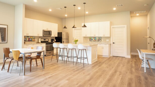 A modern kitchen with white cabinets, a central island with stools, and a dining area with a table and chairs.