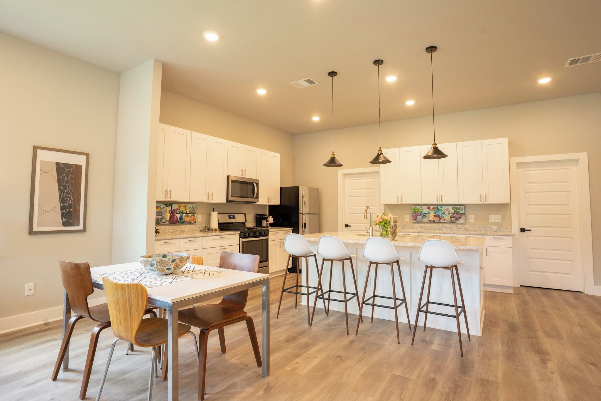 Una cocina moderna con armarios blancos, una isla central con taburetes y lámparas colgantes.