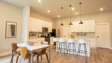 Una cocina moderna con armarios blancos, una isla central con taburetes y lámparas colgantes.