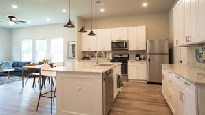 A modern kitchen with white cabinets, stainless steel appliances, and pendant lighting.