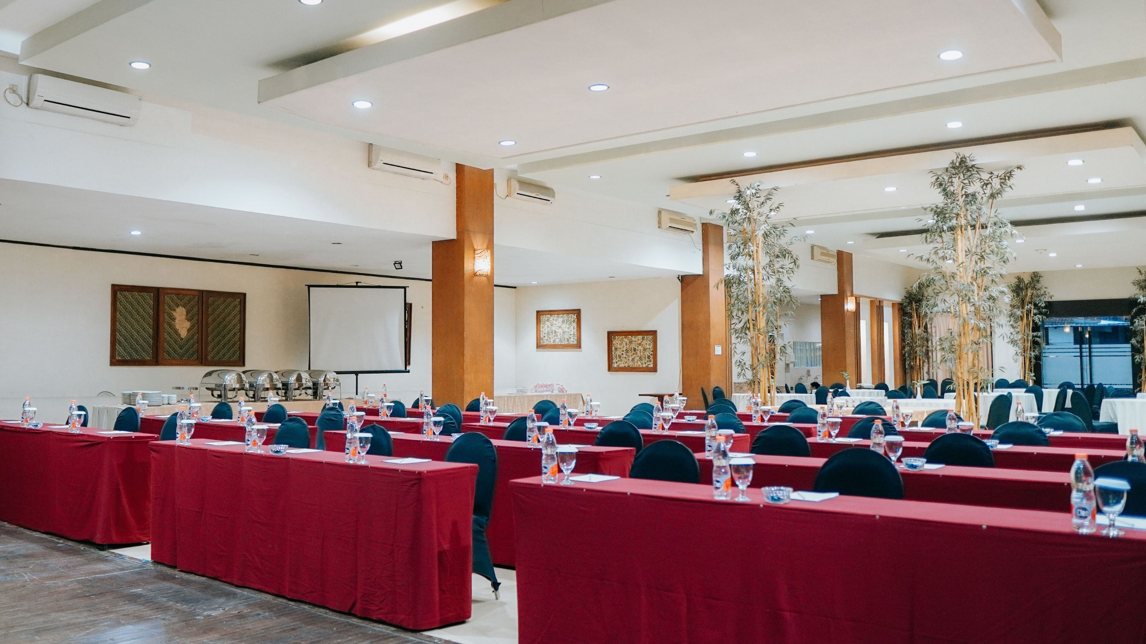 A conference room with rows of tables, chairs, and a projector screen.