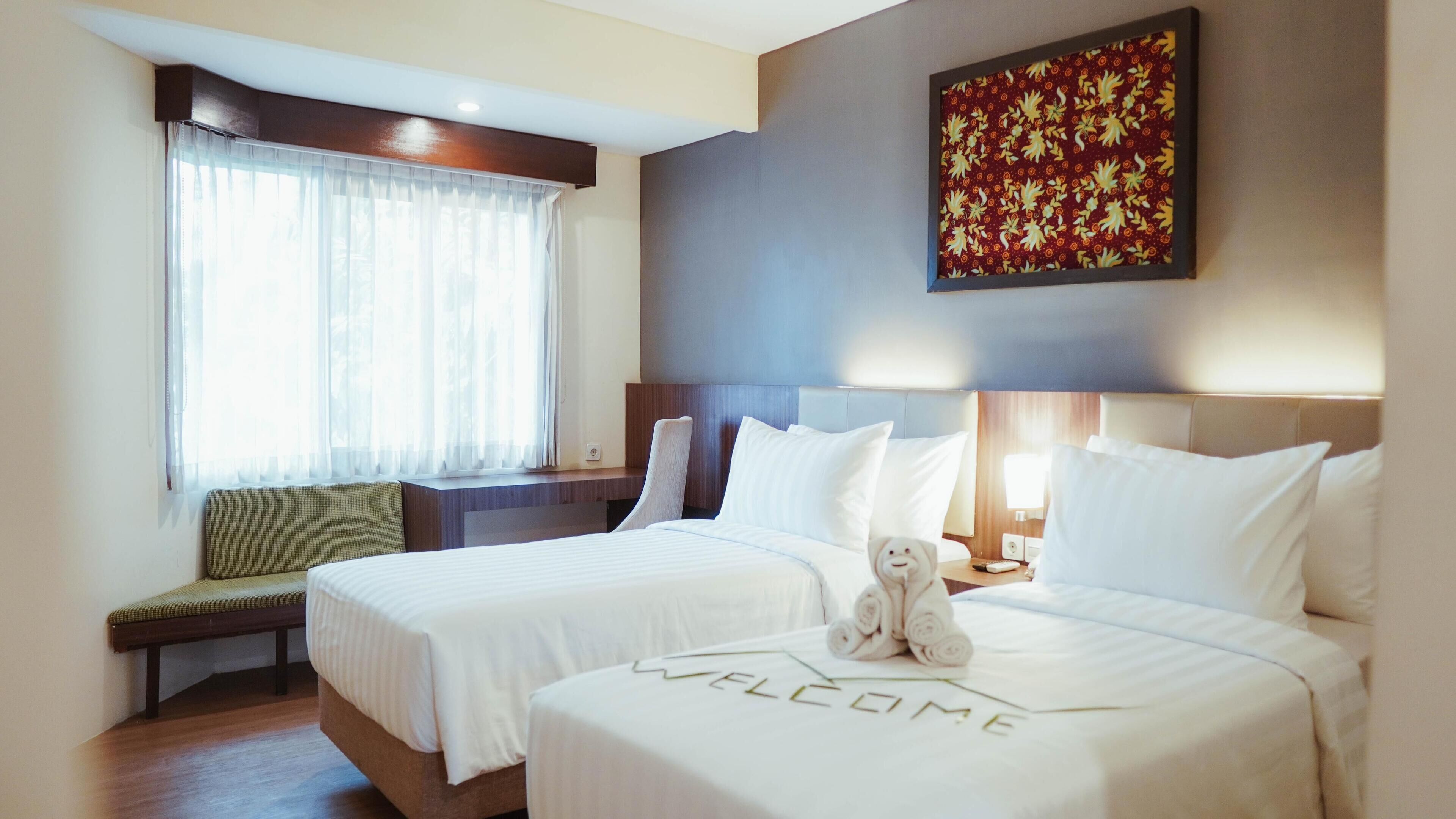 A hotel room with two beds, a bench, a wall-mounted painting, and a window with sheer curtains.
