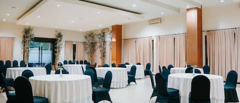Un salón de banquetes con mesas y sillas redondas, ventanas amplias y un techo alto con iluminación empotrada.