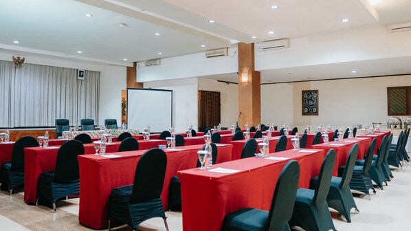 A conference room with rows of tables and chairs, a whiteboard, and an air conditioning unit on the ceiling. - Tuwuh Hotel at Kayutangan (Malang)