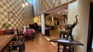 A spacious dining area with a high ceiling, checkered walls, and a central table with chairs. - Tuwuh Hotel at Kayutangan (Malang)