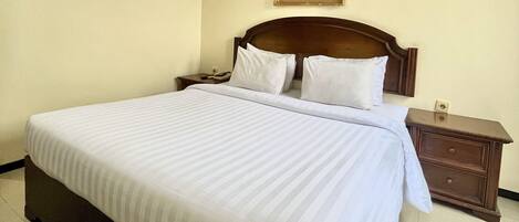 A neatly made bed with white bedding, a wooden headboard, and a nightstand with a lamp.