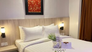 A neatly made bed with a welcome mat, pillows, and a small plant. There are two bedside tables with lamps and a framed picture above the bed. - Tuwuh Hotel at Kayutangan (Malang)