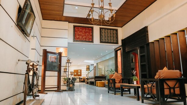 A spacious lobby with a high ceiling, a chandelier, and a seating area with sofas and a coffee table. - Tuwuh Hotel at Kayutangan (Malang)