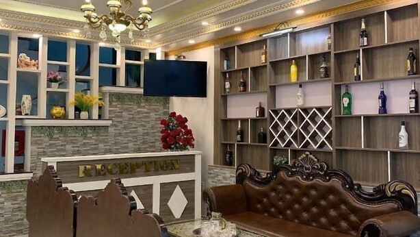 Ein luxuriöses Wohnzimmer mit einem braunen Ledersofa, einem Couchtisch und einem an der Wand montierten Fernseher. Es gibt Regale mit verschiedenen Flaschen und eine dekorative Decke.