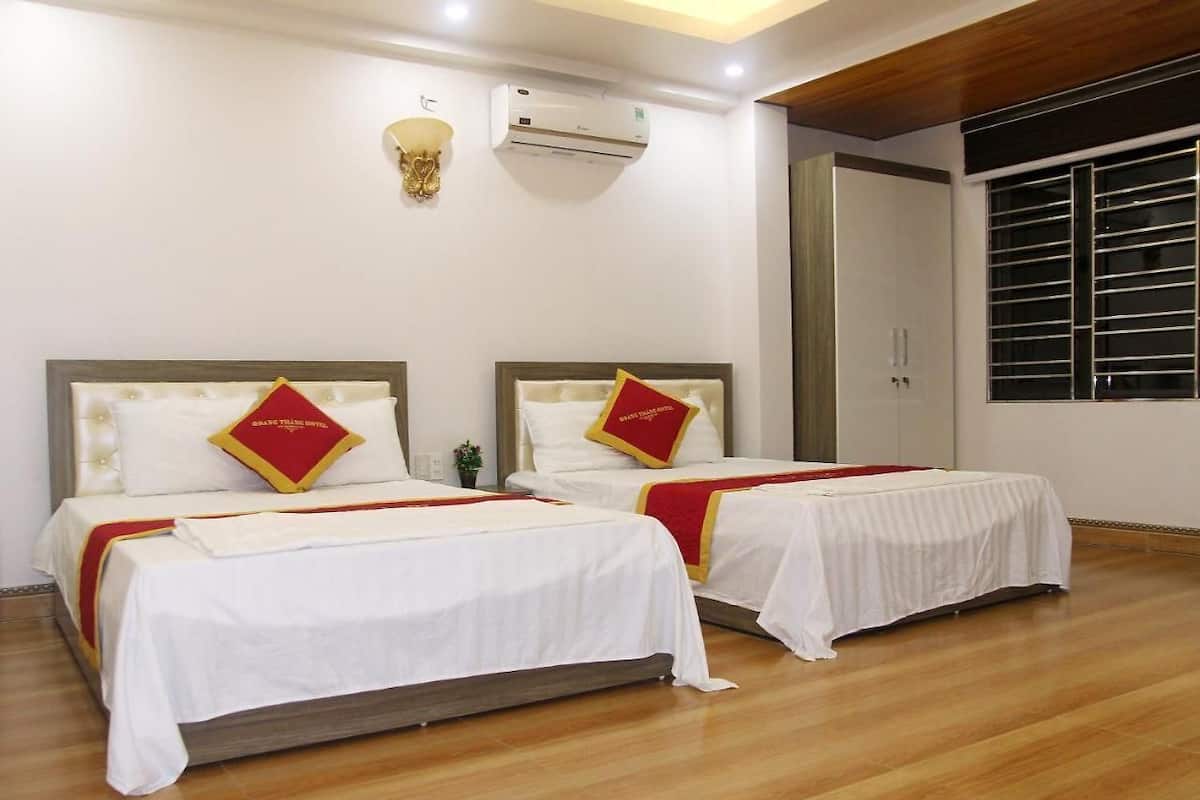 A hotel room with two beds, each with a red and white bedspread and matching pillows. There is a wall-mounted air conditioner and a window with blinds.