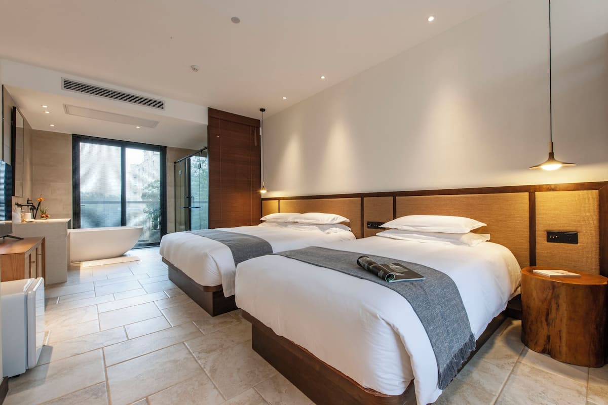 Une chambre d’hôtel moderne avec deux lits, une baignoire, un meuble-lavabo et une grande fenêtre.