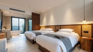 Ett modernt hotellrum med två sängar, ett badkar, en sminkbord och ett stort fönster.