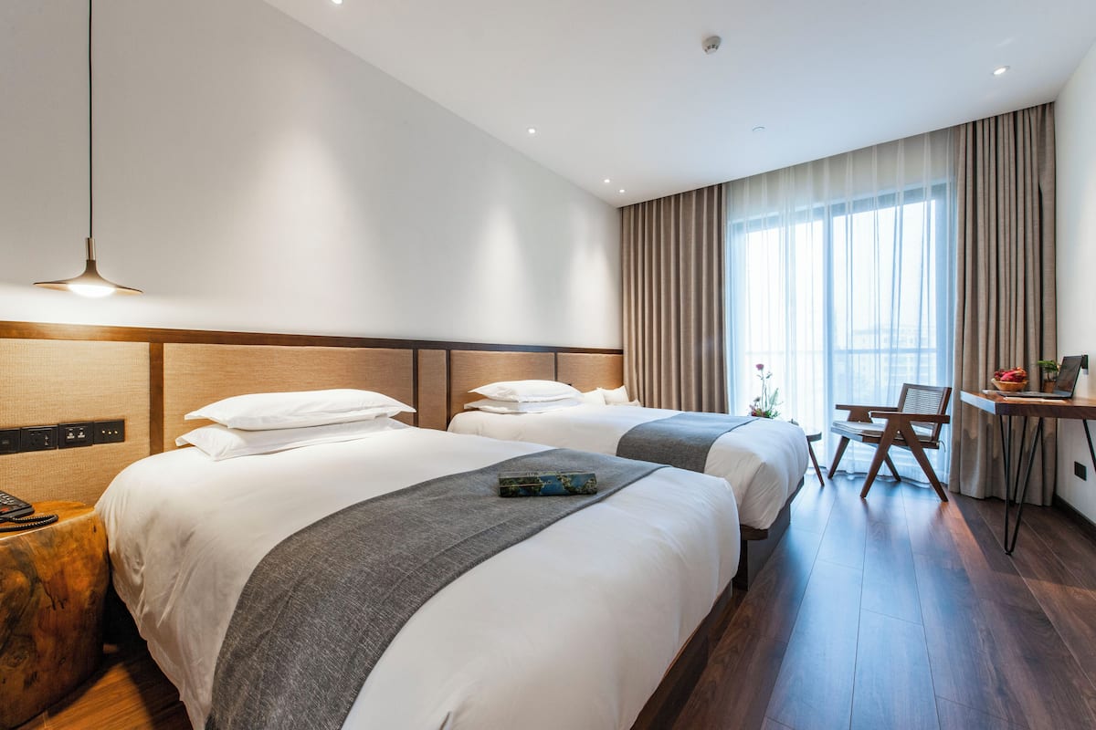 Une chambre d’hôtel avec deux lits, un bureau, une chaise et une grande fenêtre avec des rideaux.