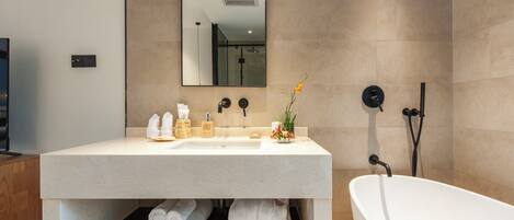 A modern bathroom with a large bathtub, a sink with toiletries, and a mirror.