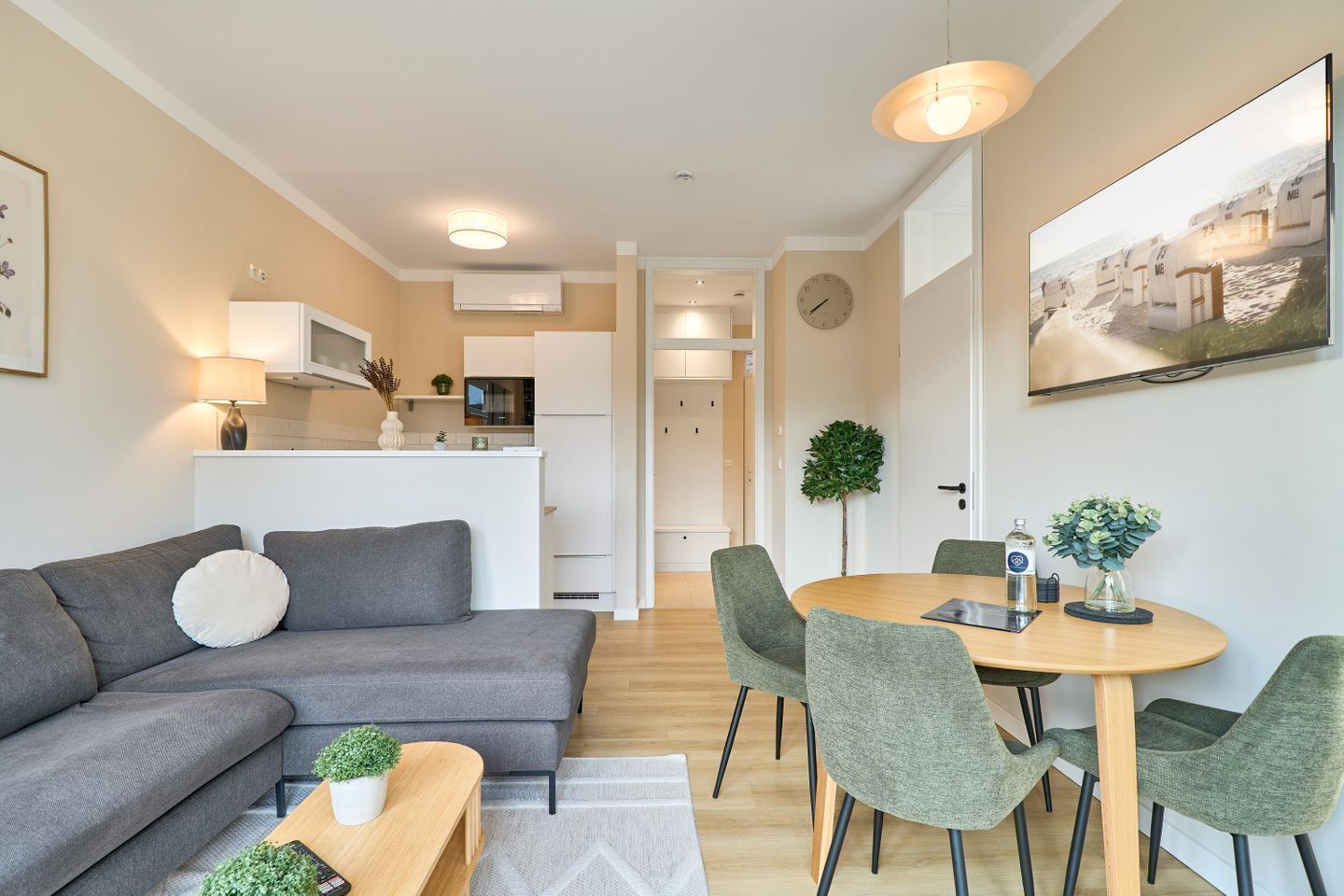 Ein modernes Wohnzimmer mit einem grauen Sofa, einem Holztisch und einem Essbereich mit rundem Tisch und grünen Stühlen.