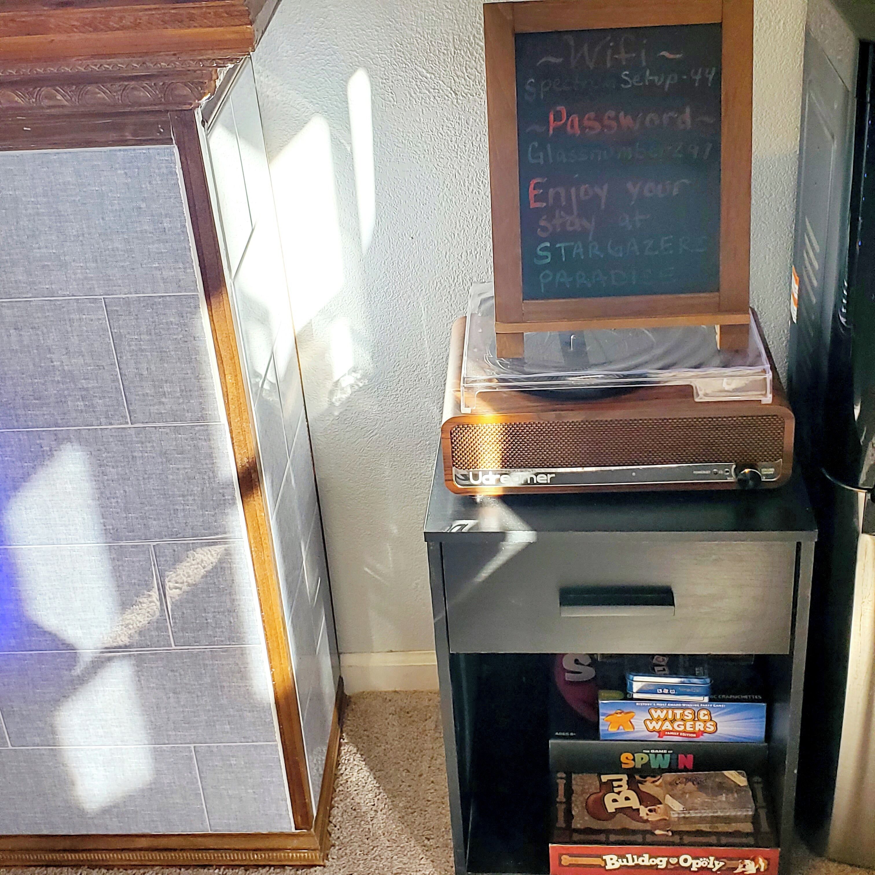A room with a chalkboard displaying WiFi details, a vintage radio, and board games like Monopoly and Scrabble.