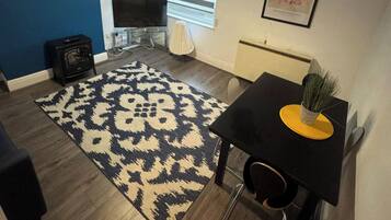 A living room with a patterned rug, a black table with a plant, a TV, and a fireplace.