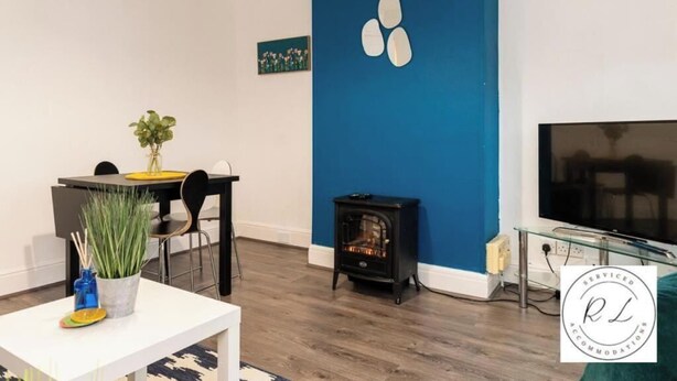 A modern living room with a blue accent wall, a fireplace, a dining area with chairs and a table, and a flat-screen TV. - 1br-2guests-freeparking-wifi-tv (Birmingham)