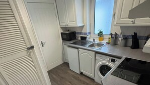 A compact kitchen with white cabinets, a microwave, a sink, and a built-in washing machine. - 1br-2guests-freeparking-wifi-tv (Birmingham)