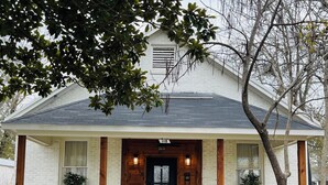 A white building with a dark roof, a black front door, and two wooden pillars.